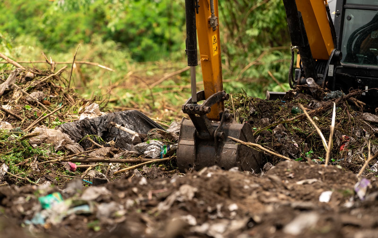 Excavator bucket digging through debris and soil on a cleared lot