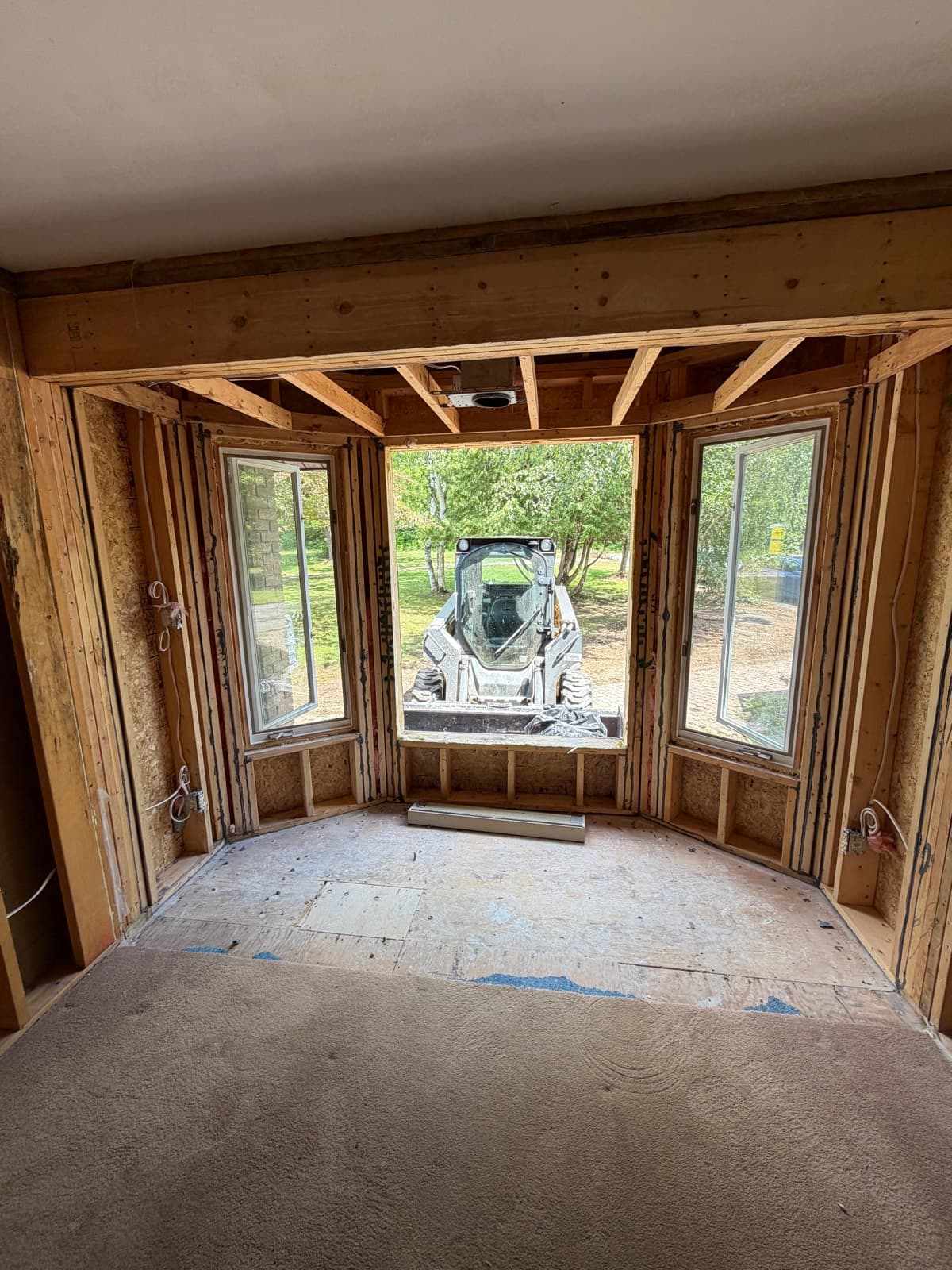 Bay-window room stripped to framing with a skid steer waiting outside