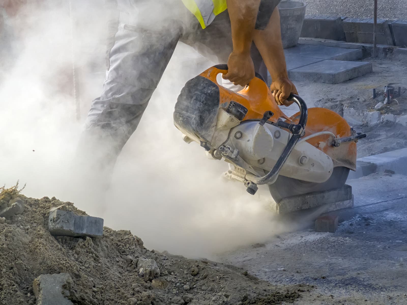 Worker cutting concrete with a gas-powered saw in a cloud of dust