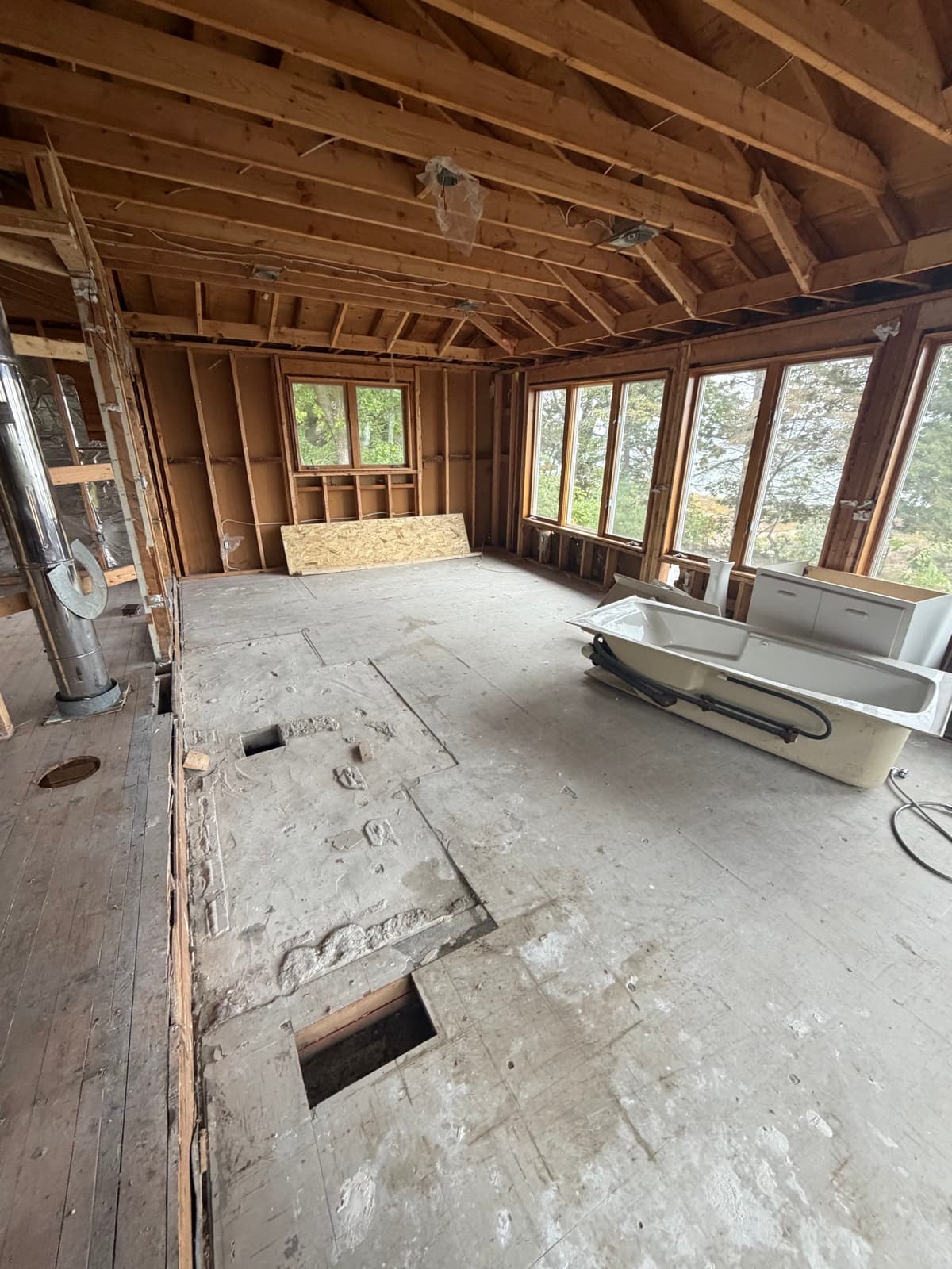 Room stripped to the studs and subfloor with a tub waiting to be removed